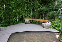 Wooden bench set on two boulders next to a pepple pool - Family Monsters Garden, RHS Chelsea Flower Show 2019
