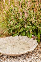 Large concrete bird bath made with a Tetrapanax leaf with metal robin and Persicaria amplexicaulis 'Rosea' - October, France.