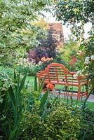 Orange garden bench with containers of Dahlia 'David Howard' viewed through border