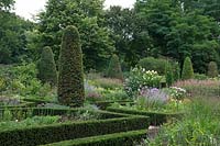 View over Buxus- Box - edged beds filled with flowers with topiary columns and trees beyond