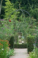 Metal arbour with Rosa - Climbing Rose - and stone urn on pedestal 
