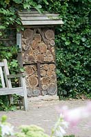 Insect hotel with roof, against a wall by path and bench