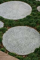 Round cast in situ concrete stepping stone, set into the ground with a planting of mini Mondo grass.