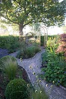 A path leads to a gazebo past  mixed borders. Early morning at 'The Homestead' an NGS garden in rural Cheshire.