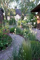 Stipa tenuissima Allium sphaerocephalon and Buxus sempervirens balls in narrow border edged by block paving leading to shed and bungalow.