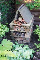A bug hotel built from wood offcuts, leftover bricks, bamboo lengths, branches, straw and pots.