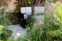 View towards a patio and dining area in small shade tolerant garden in London with a green theme. Planting includes Calamagrostis x acutiflora Karl Foerster, Dicksonia antarctica, Zantedeschia aethiopica.