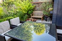 Seating and dining patio area in small shade tolerant garden in London with a green theme. Planting includes Calamagrostis x acutiflora Karl Foerster, Dicksonia antarctica.