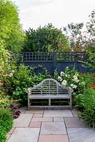 Stone patio in contemporary garden in West London with wooden seat - planting includes Helenium Moerheim Beauty, Hydrangea Vanille Fraise, Prunus Autumnalis Rosea.
