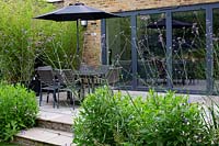 Contemporary garden in West London - view towards house and stone patio with table and parasol through borders with Verbena bonariensis.