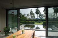 View out through open sidling doors to modern pool in contemporary garden. 