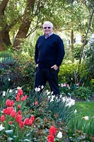 Man standing in garden near bed of flowering Narcissus - Daffodil and Tulipa - Tulip