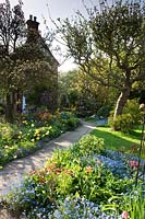 View across country-cottage style garden with borders full of flowering bulbs and perennials
