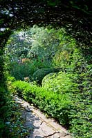 View through clipped Taxus - Yew - arch to Buxus - Box - balls and edging in border 