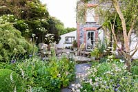 Borders planted with blues, purples and pinks including Allium 'Firmament', Valeriana officinalis, Linaria purpurea 'Canon Went', astrantias and geraniums with deck and house beyond at Sea View, Cornwall, UK in June.