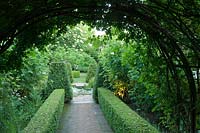 View of formal topiary in garden from under rose arch. 