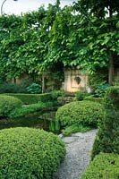 Pond in formal garden with clipped, topiary growing at the margins. 