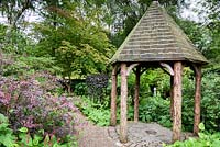 The rustic folly with tree trunk columns and slate roof tiles at York Gate Garden, Adel in July