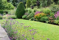 Front garden with a line of Verbena bonariensis between paving and lawn beside a border of rich oranges and pinks including heleniums, lythrum, alstroemerias, eupatoriums and crocosmias at York Gate Garden, Adel in July.