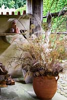 Covered open-sided potting shed with wooden stools, basket work, terracotta pots and arrangement of dried seedheads at York Gate Garden, Adel in July.