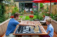 Contemporary garden in West London with stone patio and herbaceous borders, with children playing garden chess at table