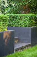 Black retaining walls with clipped Buxus - Box - hedges and brick steps mark change of level from lawn
