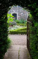 View through clipped Taxus - Yew - hedge arch, with open metal gate, to parterre garden and house