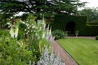 Herbaceous border, gravel path and lawn in formal garden, Taxus - Yew - hedge with arch beyond