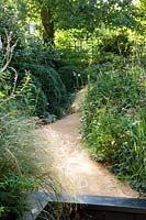 View up curved pathway with wild naturalistic borders in urban garden