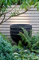 Large black feature pot surrounded by planting offerns and hostas. 