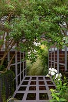 Trellis on brick wall frames garden mirror, used to disguise boundary in a small garden. Osmanthus Burkwoodii multistem in black container nearby