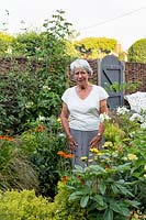 Woman standing in flower bed of a small cottage garden
