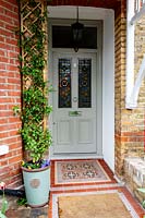 Spring front garden in West London - front door with Stained glass and Victorian style path. Trachelospermum jasminoides in container