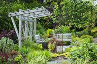 Shade structure over garden bench surrounded by perennials including Euphorbia, Carex and Alchemilla mollis - Bellevue Botanical Garden