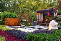 Pavilion style Chinese garden, with a freestanding water feature, moongate, stepping stones, striped paving , limestone rock garden feature, printed glass panels, steps and red lanterns.