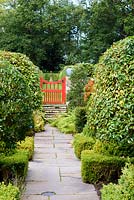 Path leading to a red painted gate passes evergreens including Portugese laurel, yew, box, holly and pyracantha at Broadwoodside, Gifford, East Lothian in Scotland.
