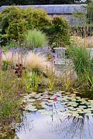Naturalistic pool in a rural garden surrounded by planting including Dierama pulcherrimum, Stipa tenuissima and Aster x frikartii 'Monch'.