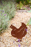 Cut out metal hen in a gravel garden.