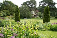 A view of Abbeywood House, an Edwardian residence built in 1908, seen accross a herbaceous border with  Allium cristophii Achillea 'Moonshine'and Phlomis russeliana and repeated conifers.