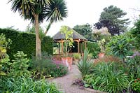 The Exotic Garden at Abbeywood Gardens. Beds contain plants including Salvia coccinea 'Lady in Red' Bergenia Hemerocallis Cordyline australis and Phormium