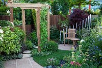 Pergola, with hexagonal paving and seating area, set amongst herbaceous plants in the 1970's Anniversary Garden at BBC Gardener's World Live 2017.