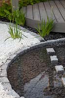 White gravel, contrasting with circular grey decking and circular pond edged with granite setts in the 'Serenity' garden at BBC Gardener's World Live 2017