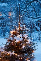 Winter decorations - christmas tree with lights and snow in the garden