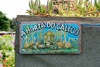 A Horta Do Galeco or Galeco's Vegetable Garden a painted sign on side of shed showing a lady feeding livestock with oversized onions growing, Fulham Palace Allotments, London.