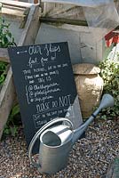 Blackboard with list of dos and don'ts and watering can, Skip Garden, Kings Cross, London, UK.