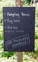 Board advertising property portfolio for Hedgehog House, Bug Hotel, Bird Box and Earwig Hotel, Priory Common Orchard Community Garden, London Borough of Haringey.