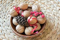A festive table centrepiece with Juglans regia, a pine cone, red ribbon and berries
