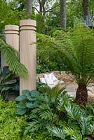 Dicksonia Antarctica Tree fern stands over circular stone sunken seating area surrounded by stone columns. The Time In Between by Husqvarna and Gardena - RHS Chelsea Flower Show 2015. Sponsor: Husqvarna and Gardena.