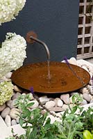 Water feature with copper pipe and bowl surrounded by pale pebbles