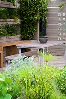 Outdoor room with table and chairs and planting of herbs and vegetables - The Year of Green Action Garden - RHS Hampton Court Palace Garden Festival 2019. Sponsors: Defra.